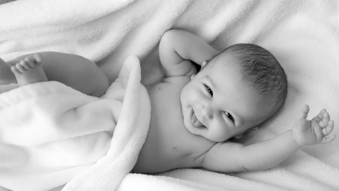 smaidošs zīdainis gultiņā, melnbalts attēls