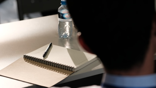 Darba galds, uz kura ir bloknots ar pildspalvu un ūdens pudele. Semināra attēls.