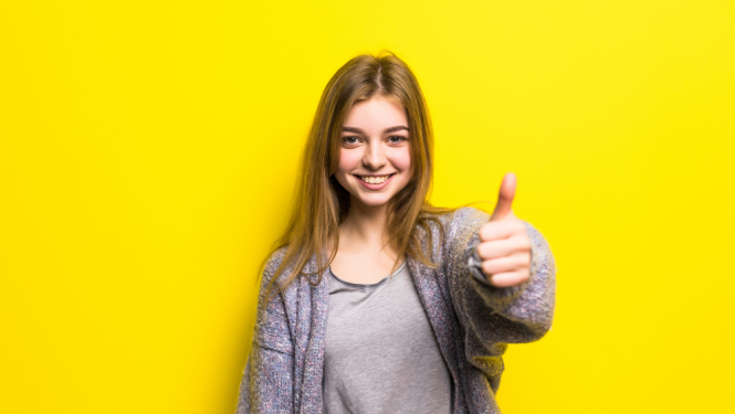 Jauna sieviete ar paceltu īkšķi uz dzeltena fona