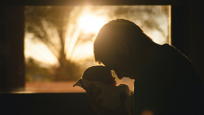 VĪrietis tur rokās zīdaini, fonā logs