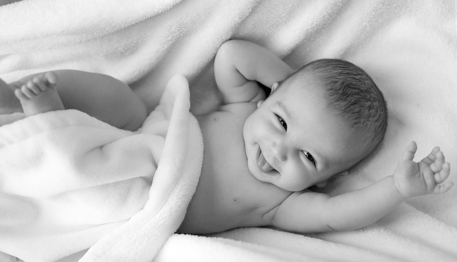 smaidošs zīdainis gultiņā, melnbalts attēls