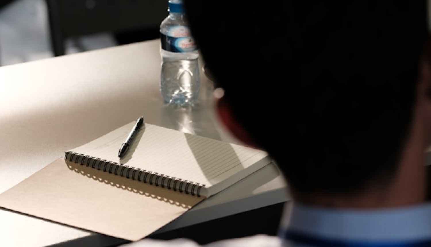 Darba galds, uz kura ir bloknots ar pildspalvu un ūdens pudele. Semināra attēls.
