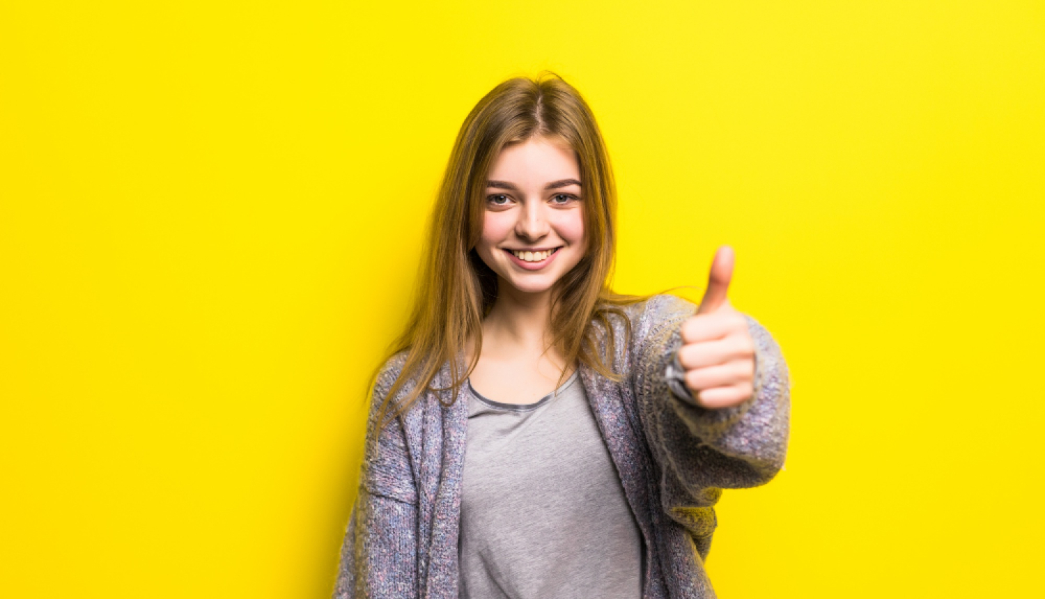 Jauna sieviete ar paceltu īkšķi uz dzeltena fona