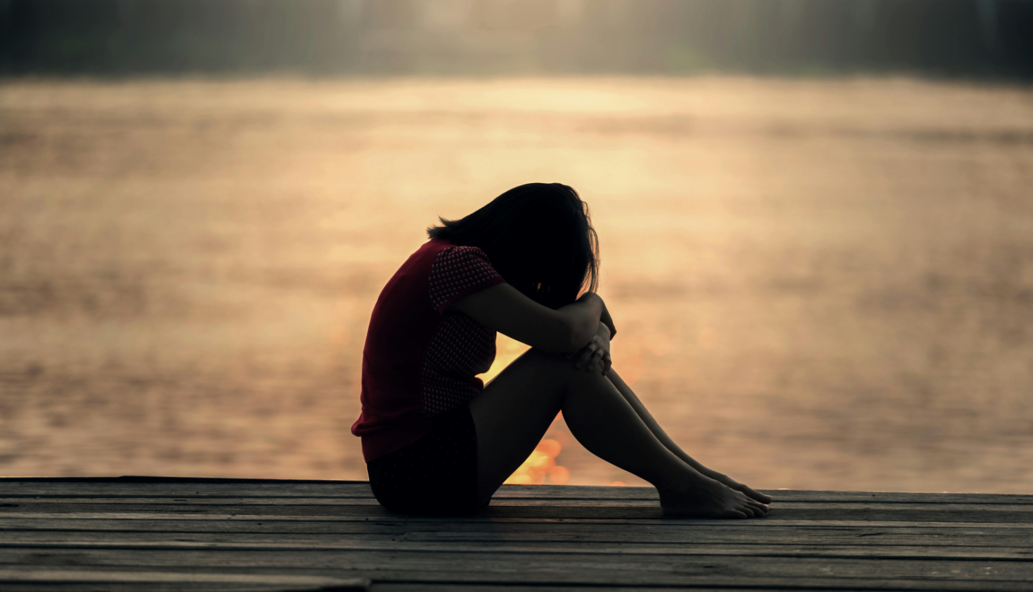 Sēdoša, skumja meitene saulrieta fonā